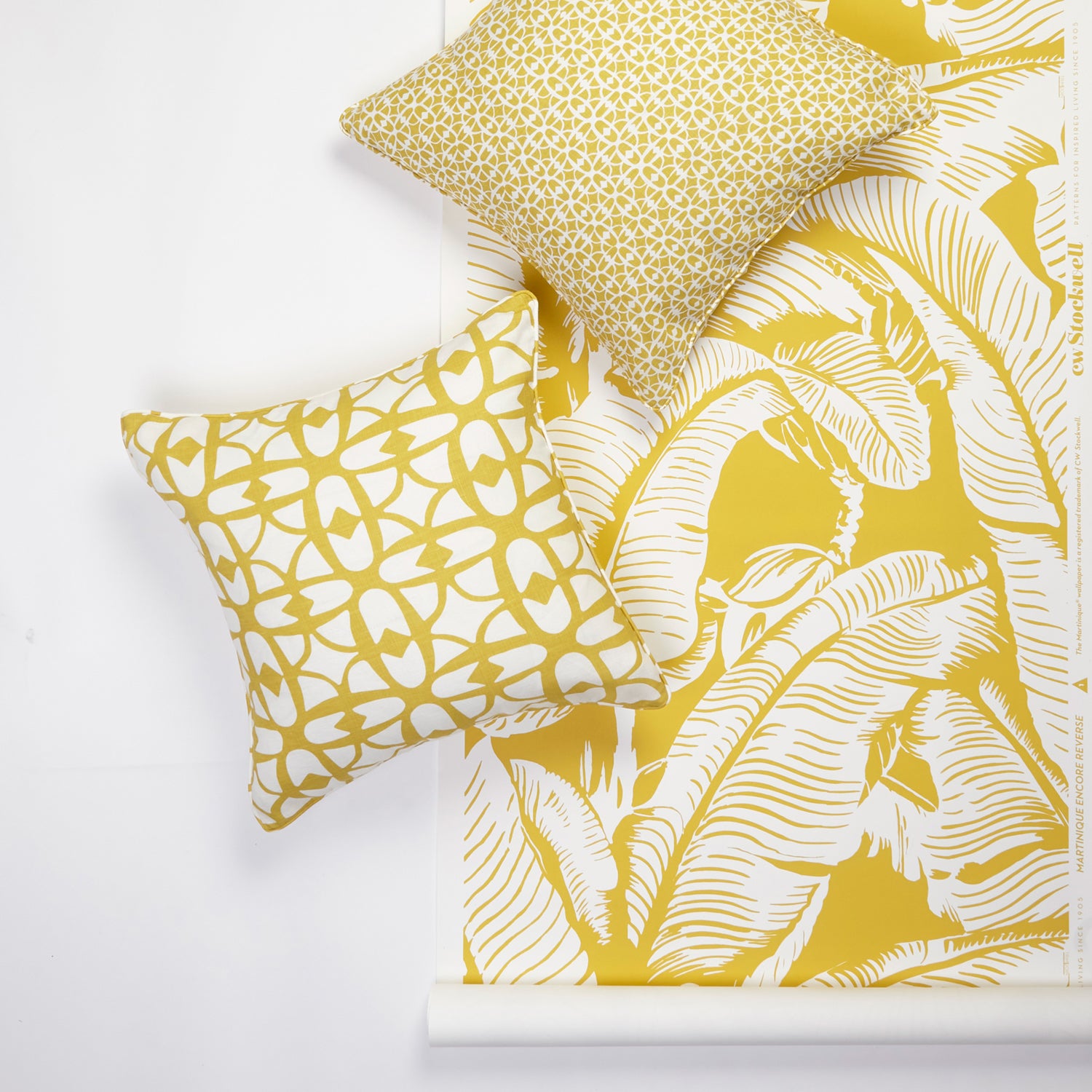 Two decorative throw pillows in yellow and white patterns, styled next to a matching yellow and white tropical banana leaf patterned wallpaper on a white background.
