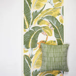 A styled flat-lay of tropical leaf patterned wallpaper with a throw pillow with a bamboo stripe pattern in green layered on top. 