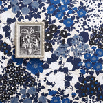 A small framed black-and-white botanical artwork with a silver-toned ornate frame, placed on top of a blue, navy, and white floral wallpaper pattern.