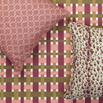 A styled flat lay with decorative throw pillow in mauve pink medallion print, animal print pillow in plum purple and olive green against a basketweave plaid wallpaper in pink, plum, tan and olive green. 