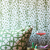 Close up image of a green lattice print throw pillow with gold side table, pink martini and stack of dice against a green and aqua blue leopard print wallpaper. 