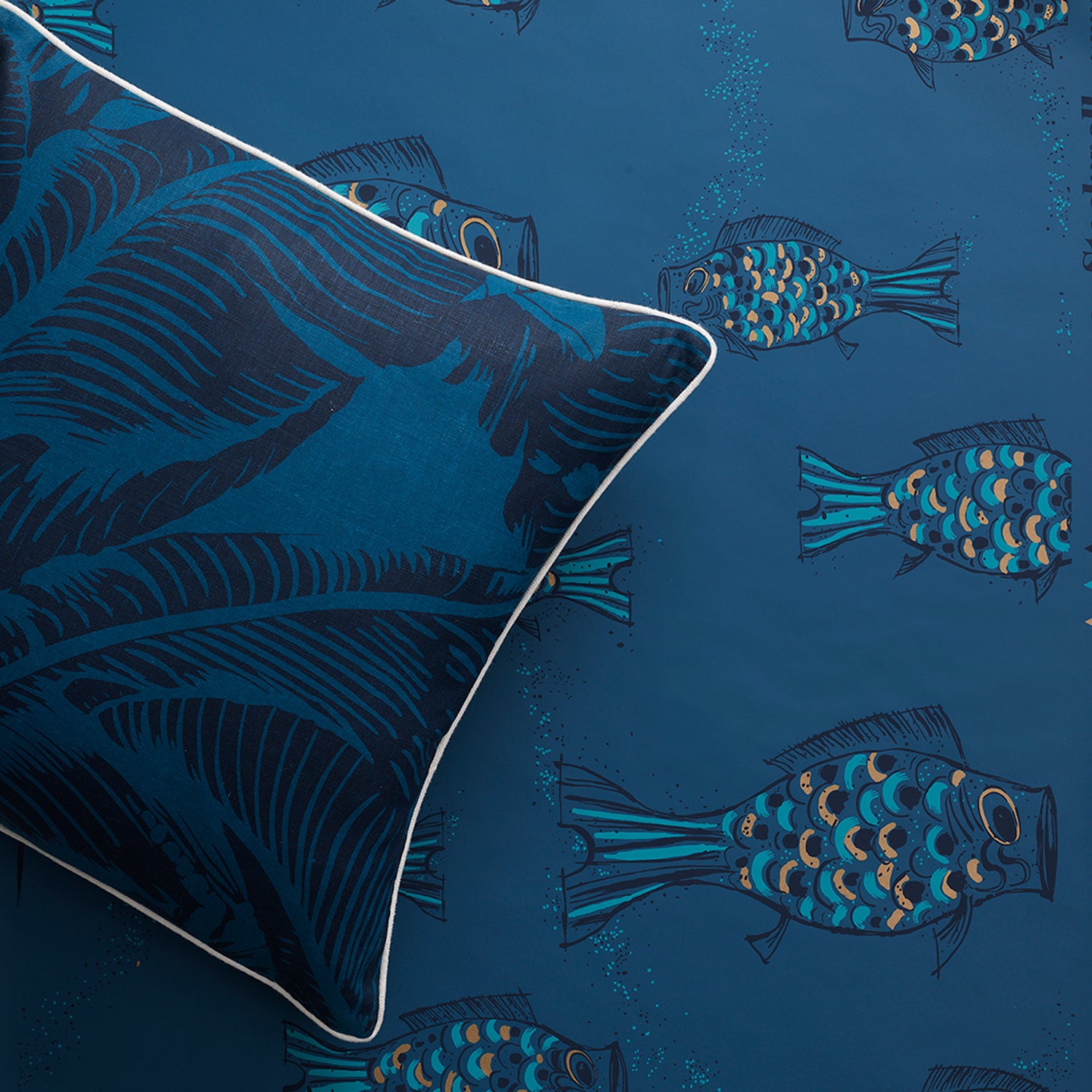 Styled flatlay with a dark blue banana leaf throw pillow atop a playful fish wallpaper in dark blue. 