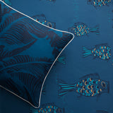 Styled flatlay with a dark blue banana leaf throw pillow atop a playful fish wallpaper in dark blue. 