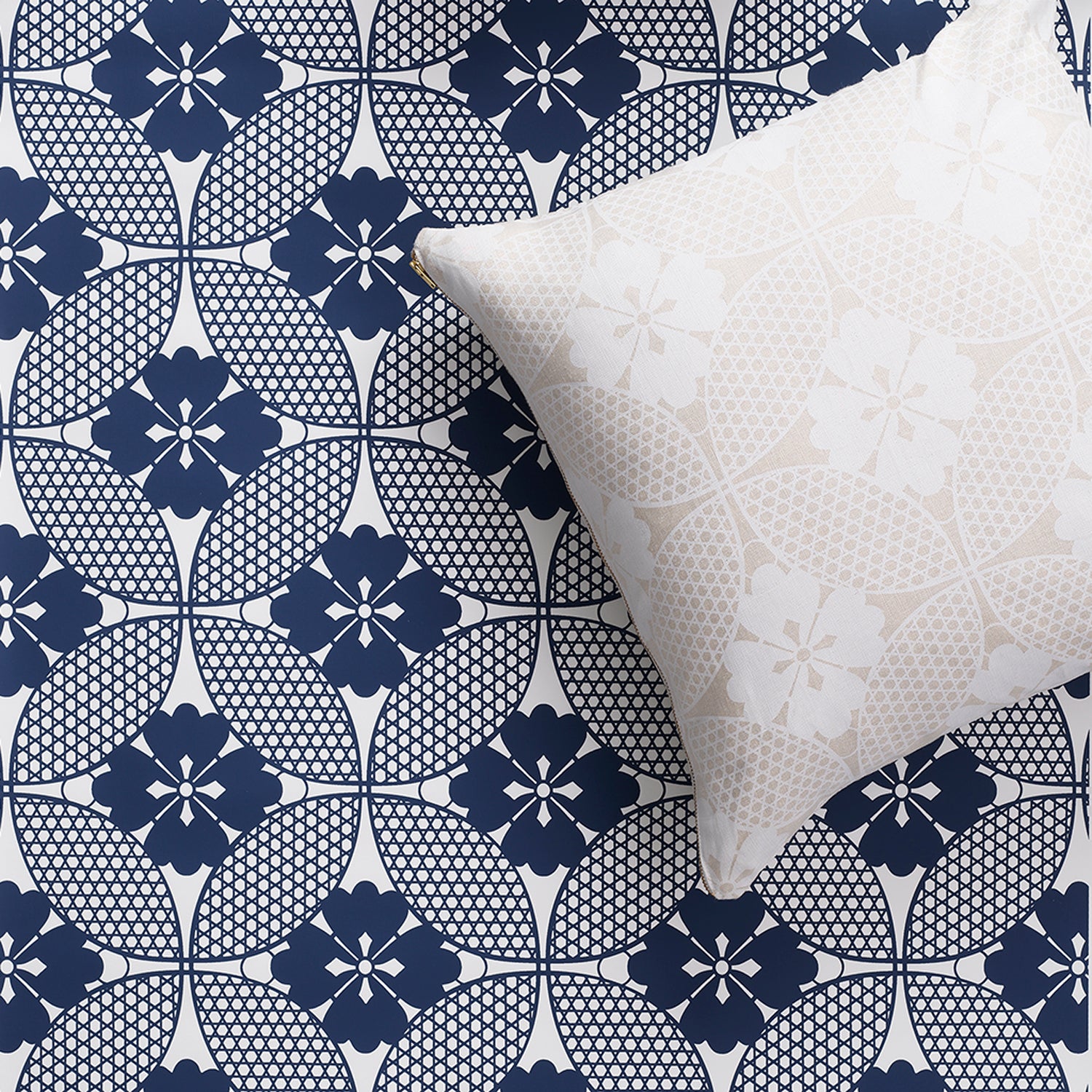 A square decorative throw pillow with a cream and beige floral lattice pattern, placed on top of a matching pattern wallpaper in blue and white. 