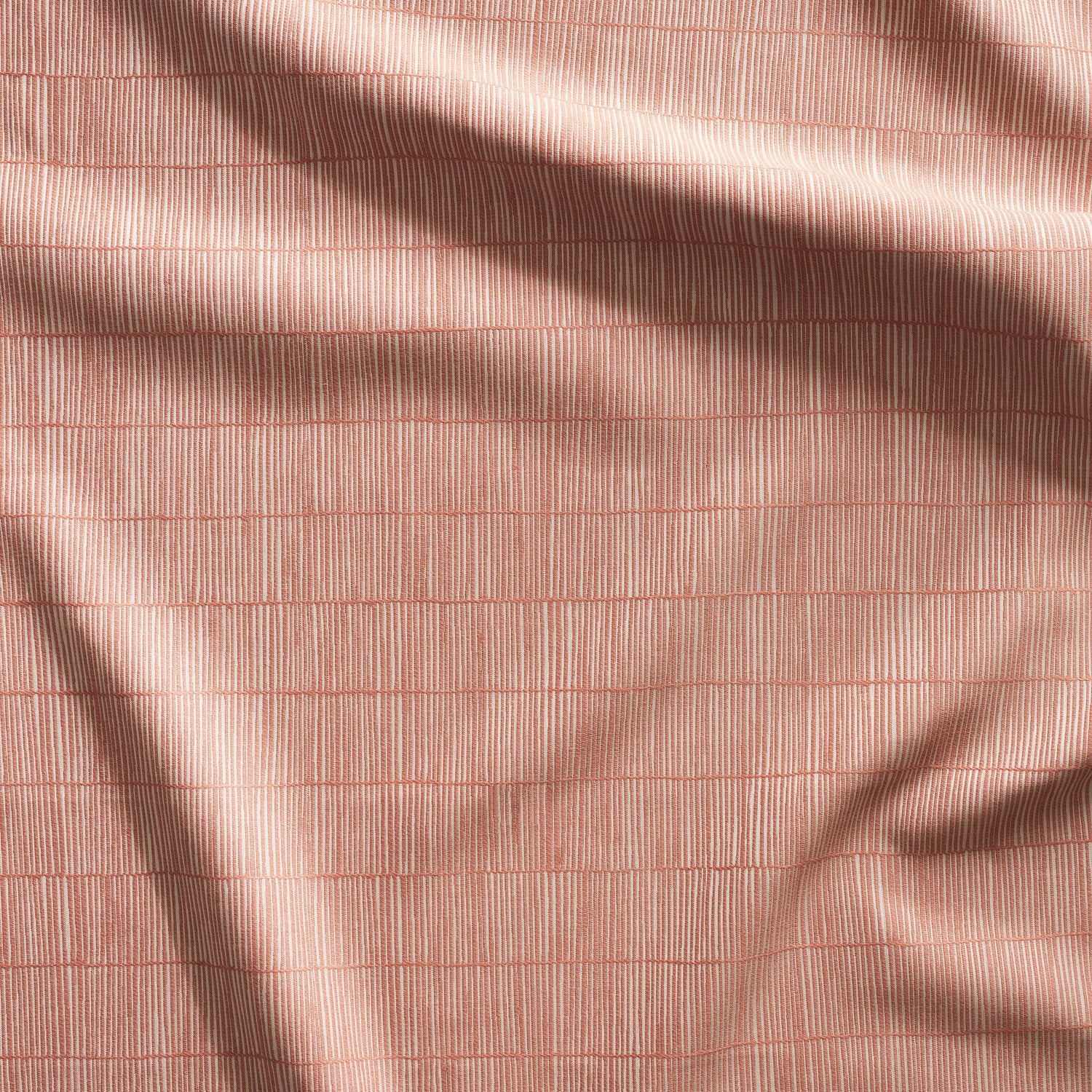Close up of gently draped woven Indoor-Outdoor fabric with thin hand drawn stripe grid in beige on coral.