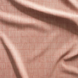 Close up of gently draped woven Indoor-Outdoor fabric with thin hand drawn stripe grid in beige on coral.