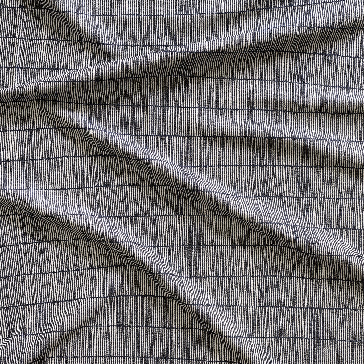 Close up of gently draped woven Indoor-Outdoor fabric with thin hand drawn stripe grid in ivory on navy. 