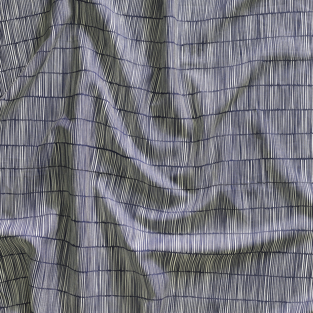 Close up of gently draped printed linen with thin hand drawn stripe grid in ivory on navy blue.