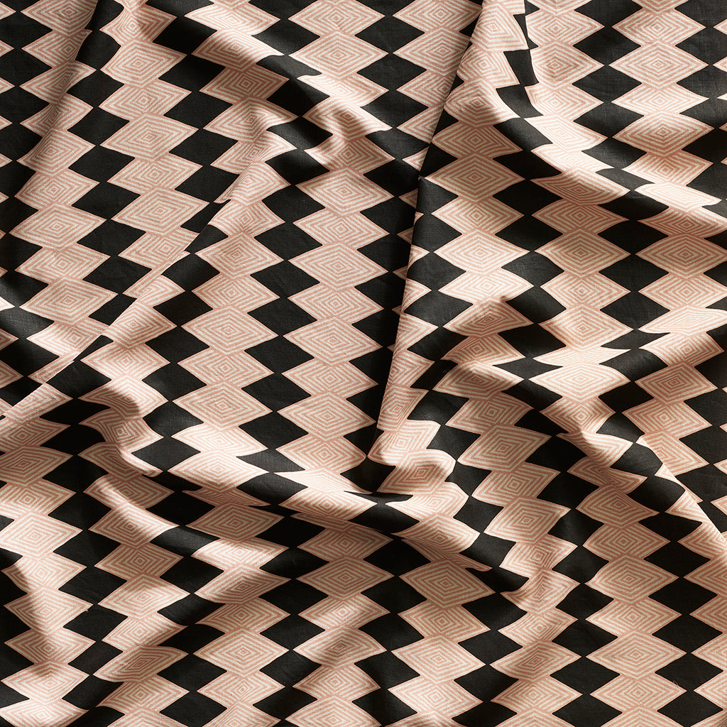Close up of gently draped printed linen with linear stacked diamond stripe in clay pink and black.