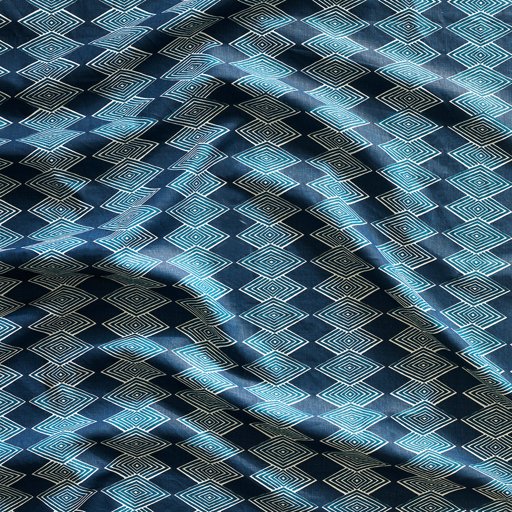Close up of gently draped printed linen with linear stacked diamond stripe in shades of navy blue.