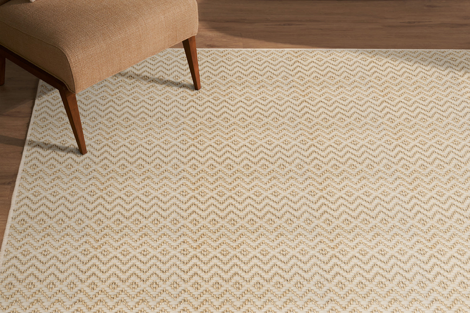 Beige patterned rug on a wooden floor with a partial view of a brown chair.