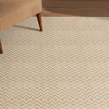 Beige patterned rug on a wooden floor with a partial view of a brown chair.