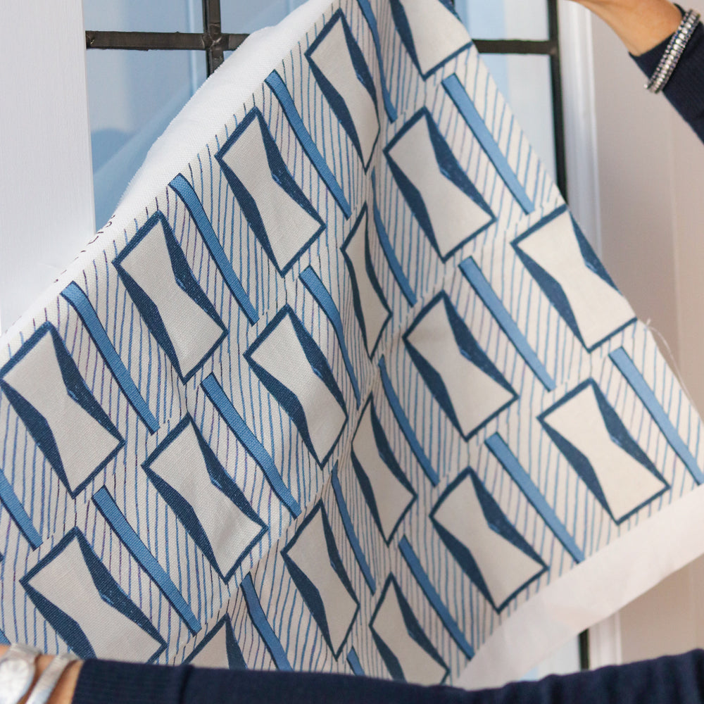 Woman's hands holding a printed fabric cutting with blue and white geometric pattern against a widow. 