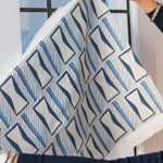 Woman's hands holding a printed fabric cutting with blue and white geometric pattern against a widow. 