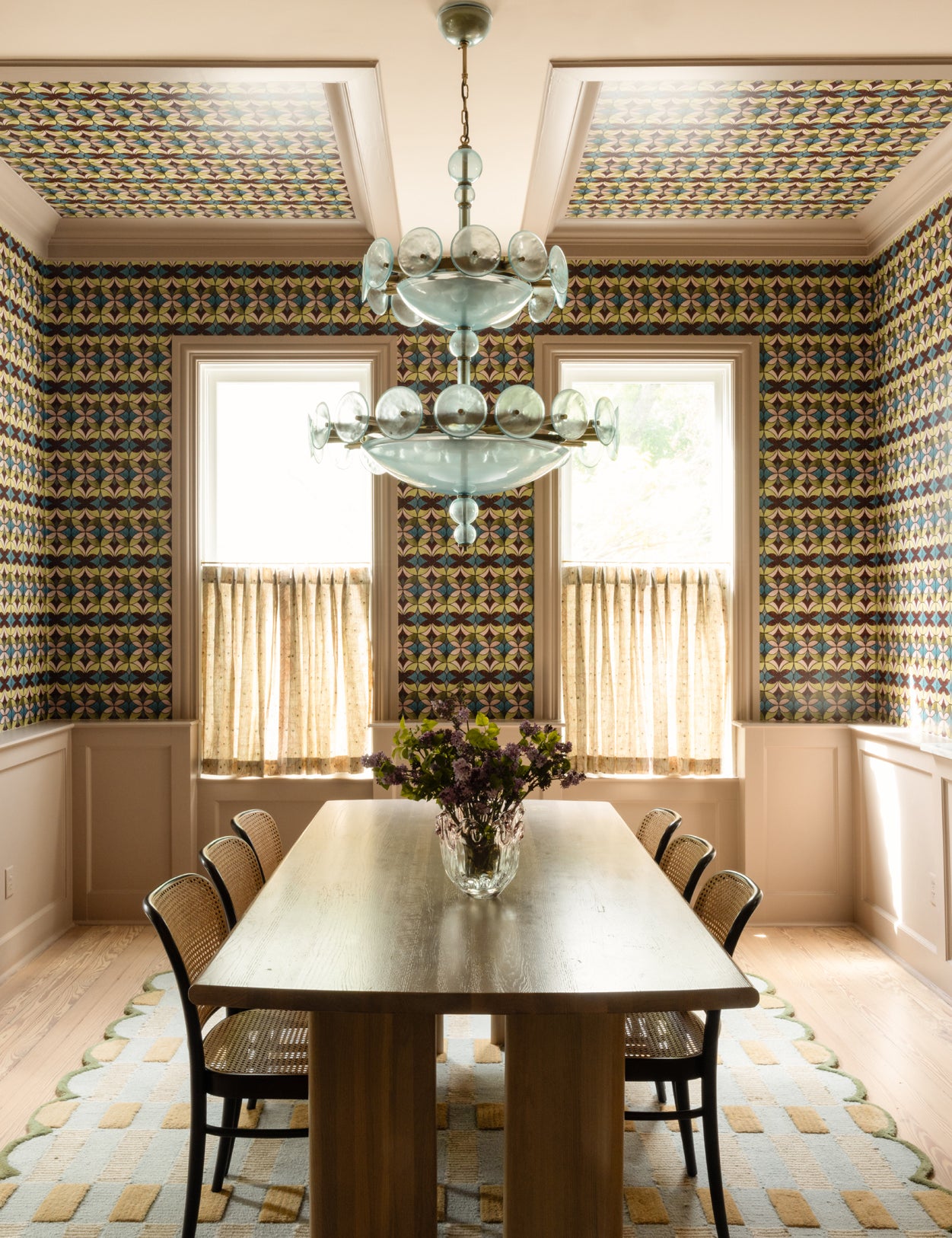 Dining room with patterned wallpaper, chandelier, and table set.
