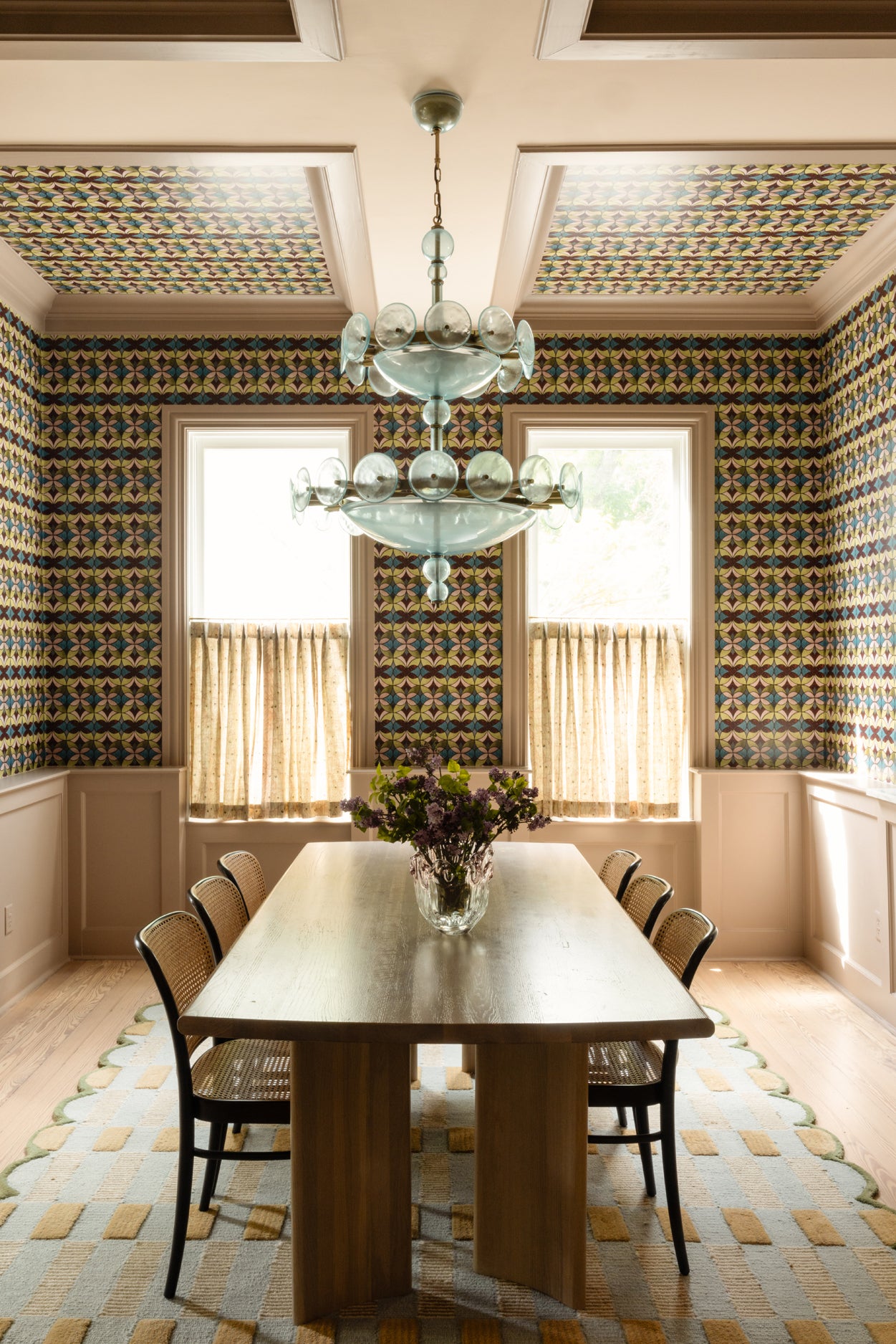 Dining room with patterned wallpaper, chandelier, and table set.