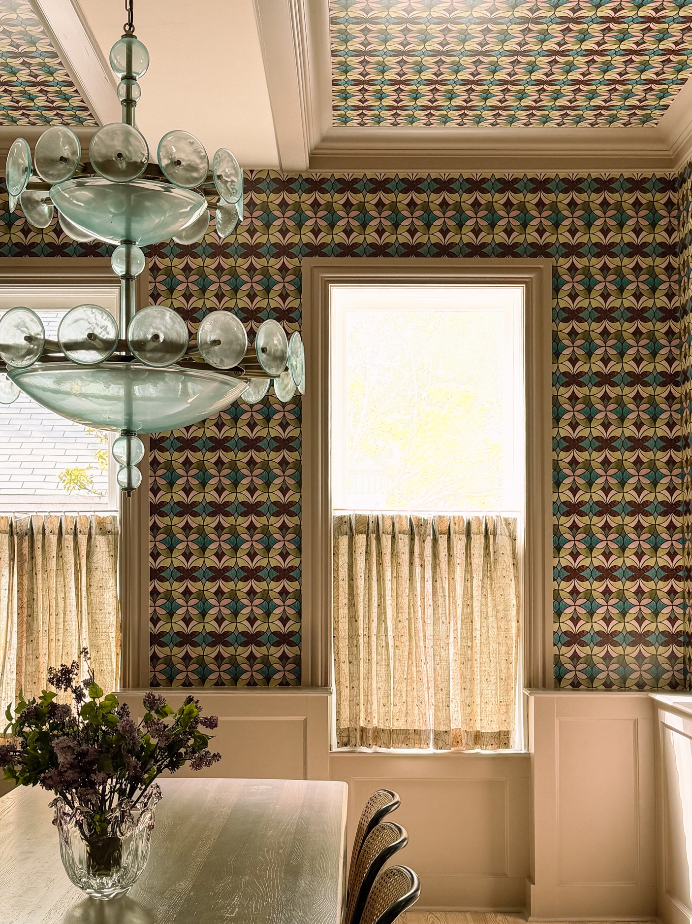 Dining room with patterned wallpaper, chandelier, and window light.