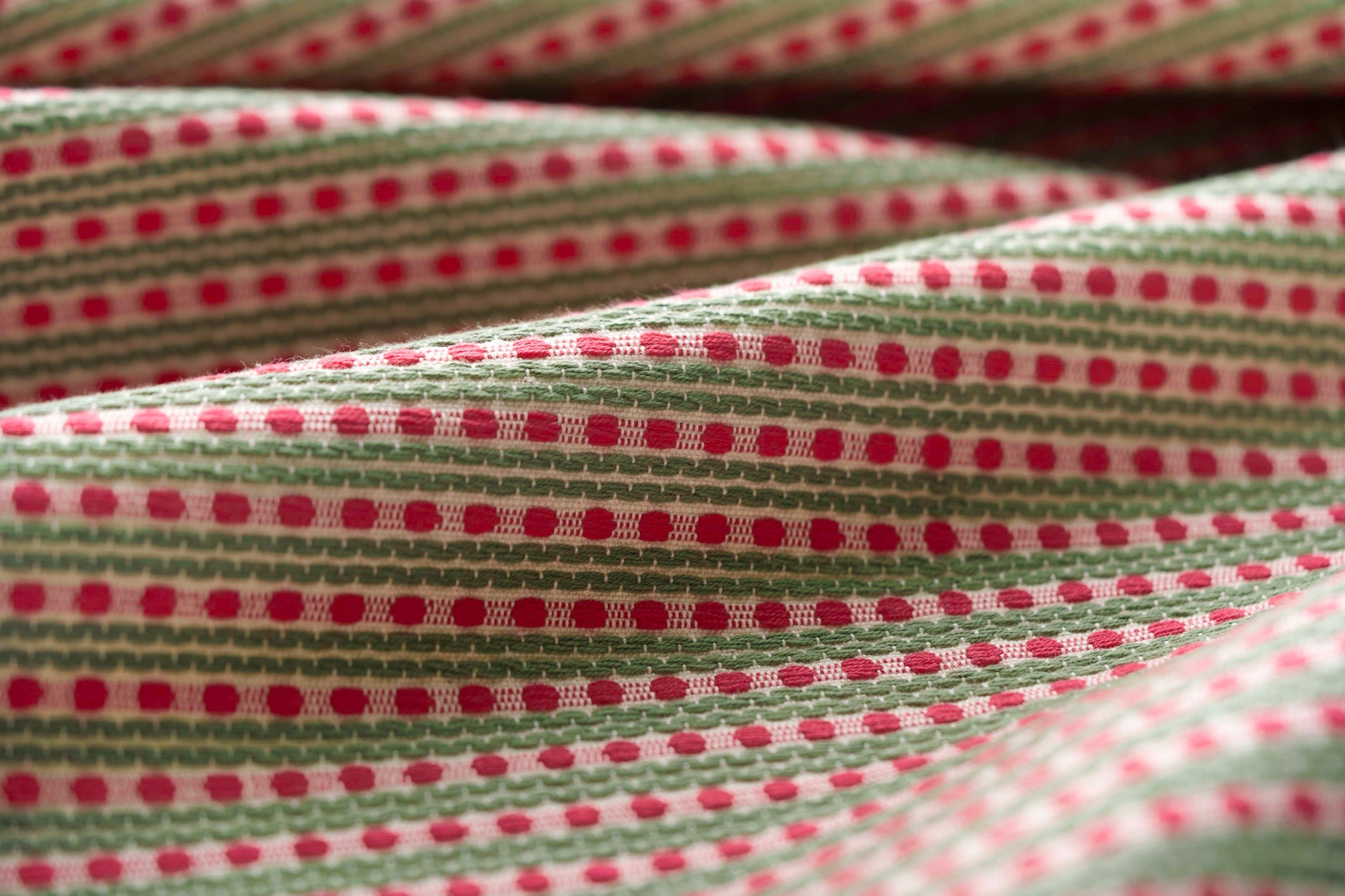 Lightly folded patterned fabric with pink dots and green stripes on a white background
