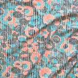 A close up of gently draped printed fabric with a pointillist abstract floral pattern in turquoise, navy blue and coral orange on white. 