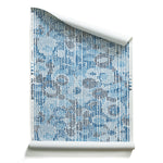 A roll of wallpaper with a pointillist abstract floral pattern in shades of blue on white. 