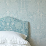 Bed with white bedding and a decorative headboard against a patterned light blue wall.