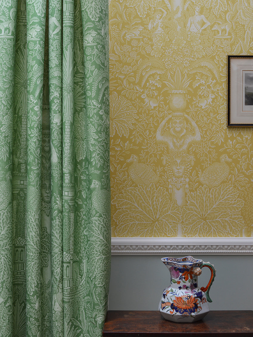 Green patterned curtain next to yellow wallpaper with a decorative vase on a table.