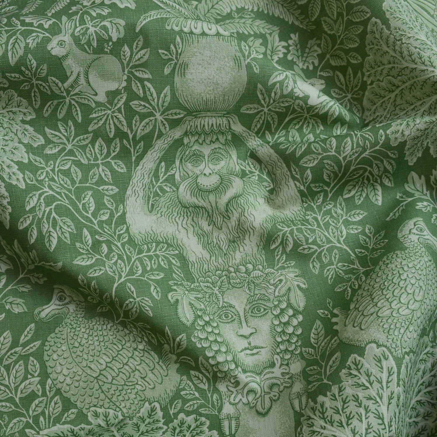 Green fabric with classical design featuring a woman's head, monkey, and peacock.