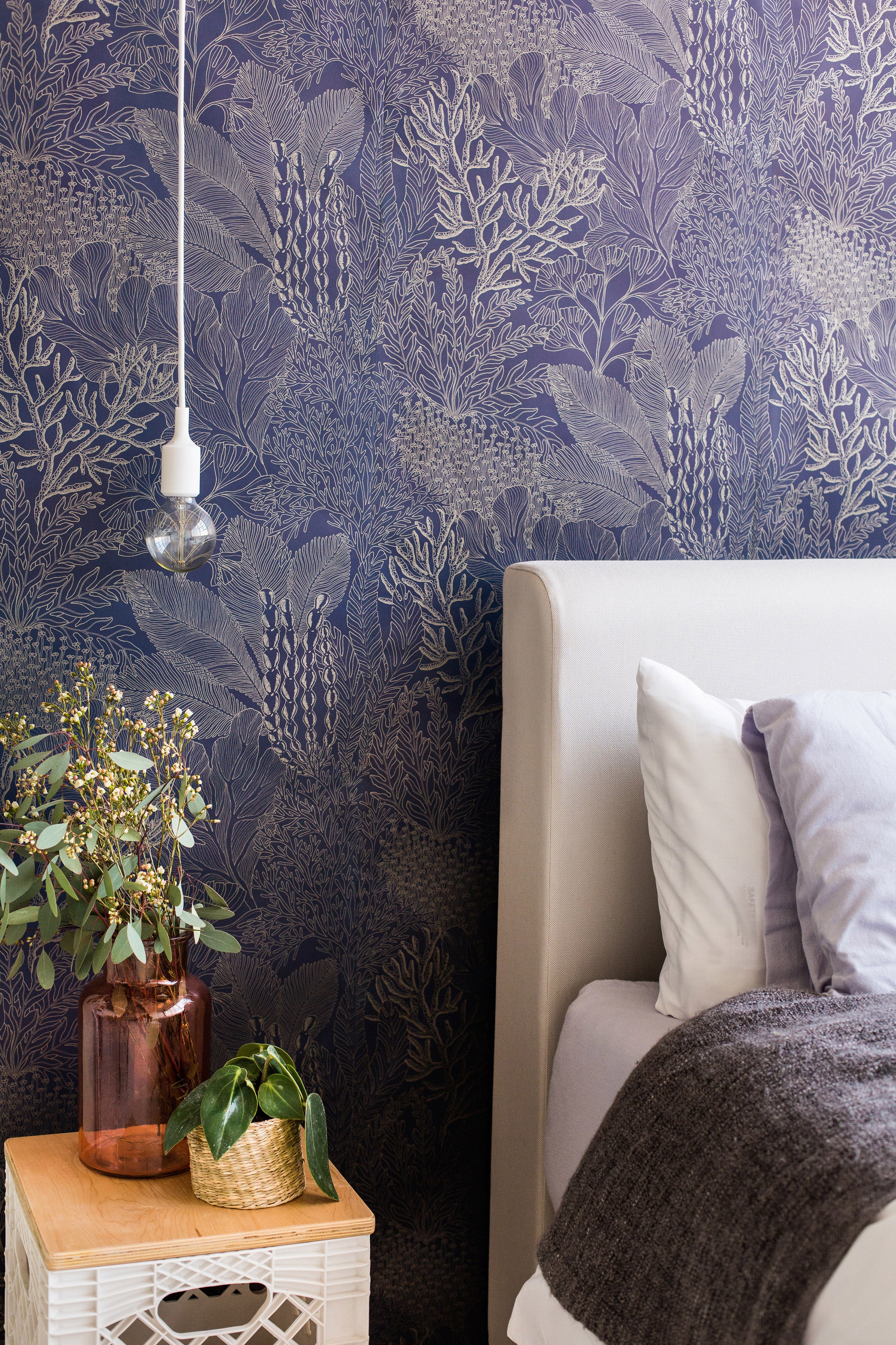 Detail of a bedroom with a statement wall papered in a dense coral print in gold on a navy field.