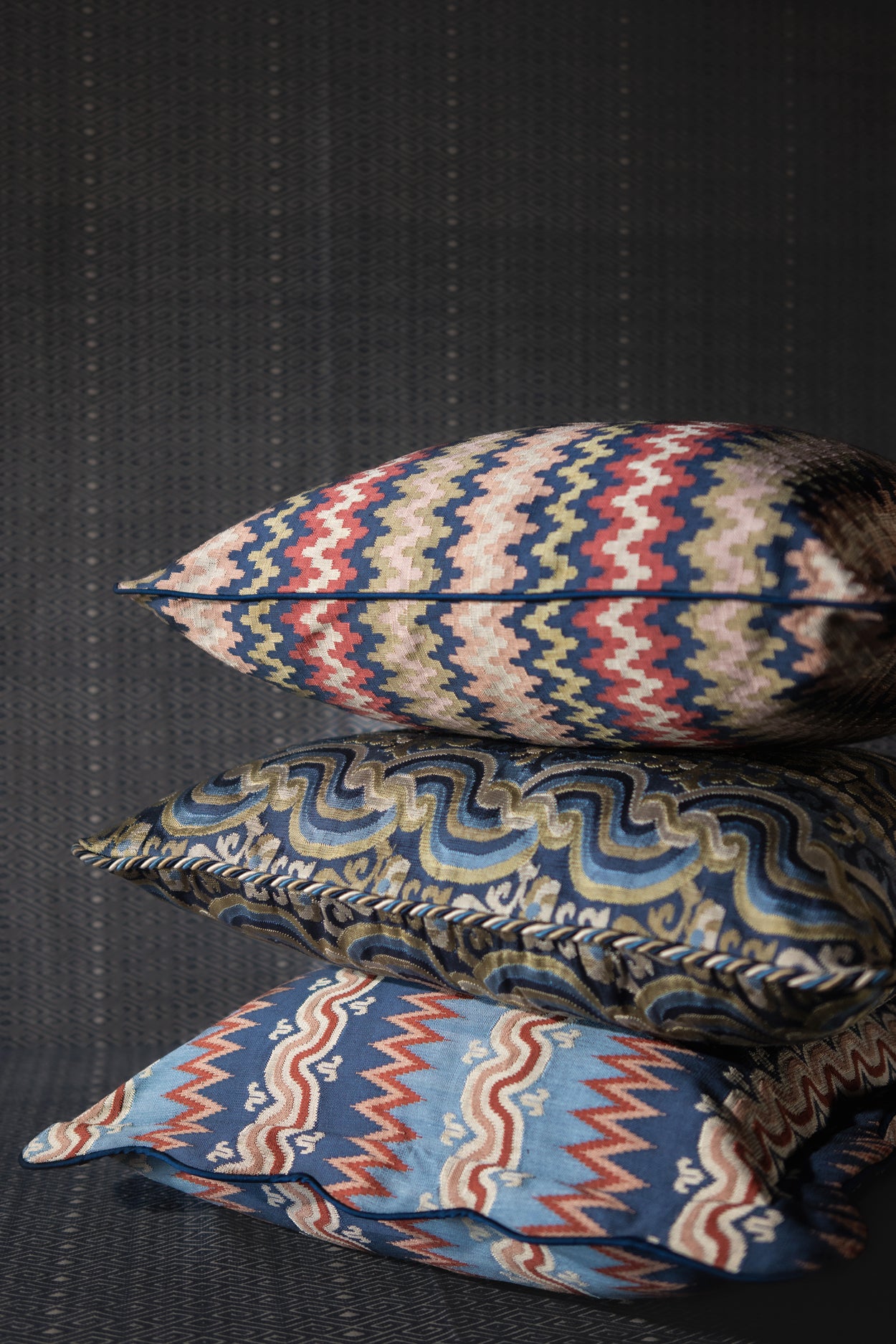 Three patterned pillows on a dark textured surface