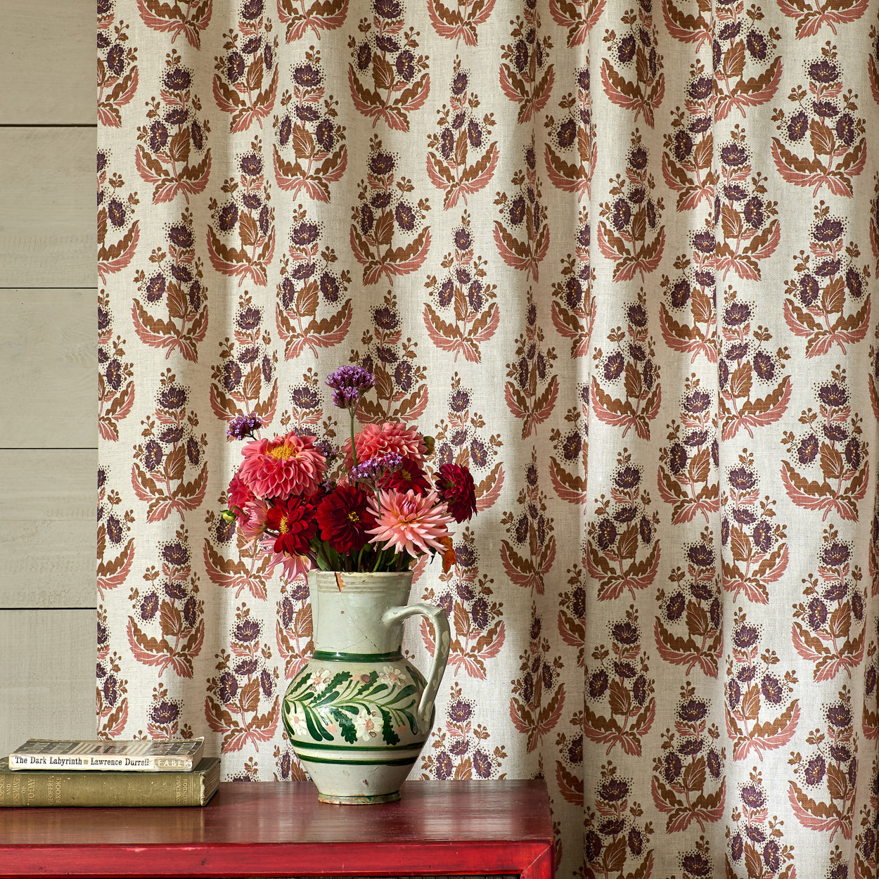 Decorative curtain with floral pattern in front of a wooden cabinet with a vase of flowers on top.