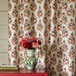 Decorative curtain with floral pattern in front of a wooden cabinet with a vase of flowers on top.