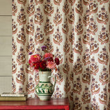 Decorative curtain with floral pattern in front of a wooden cabinet with a vase of flowers on top.