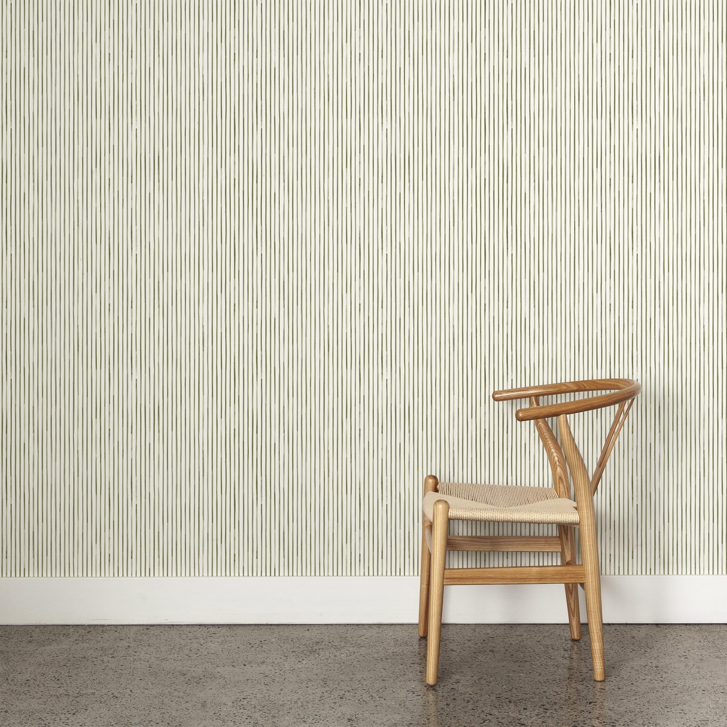 A wooden chair stands in front of a wall papered in a painterly stripe pattern in sage on a white field.