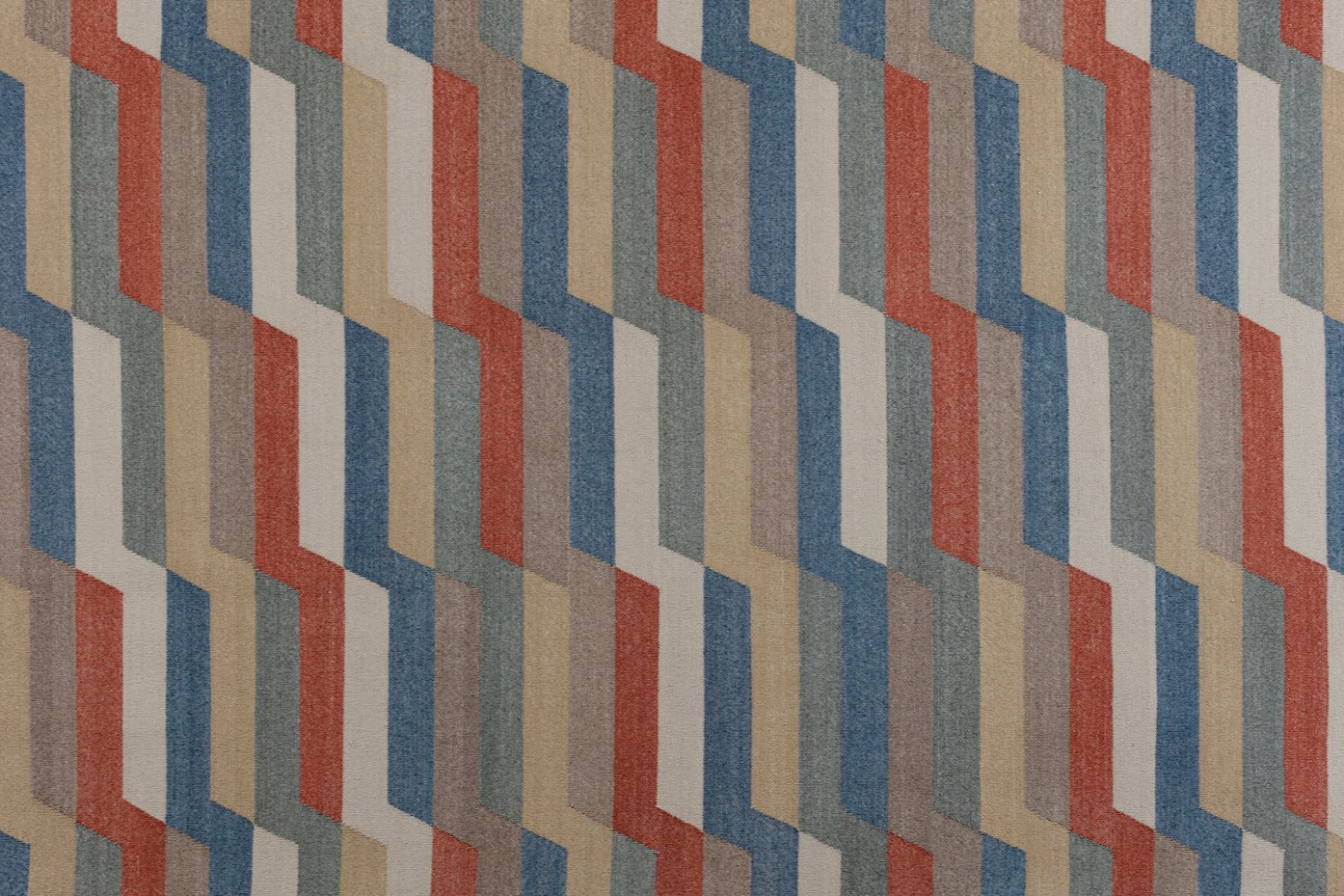 Detail of a handwoven rug with a stacked zig zag stripe in shades of blue, red, ivory, and taupe. 