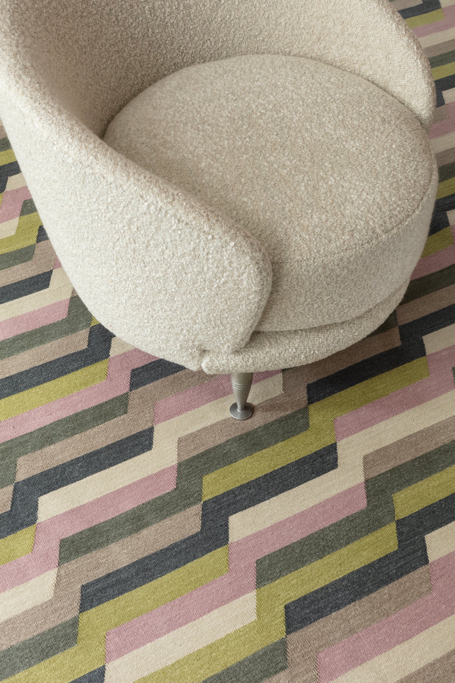 White bouclé side chair atop a handwoven rug with a stacked zig zag stripe in purple, lime green, cream and shades of grey. 