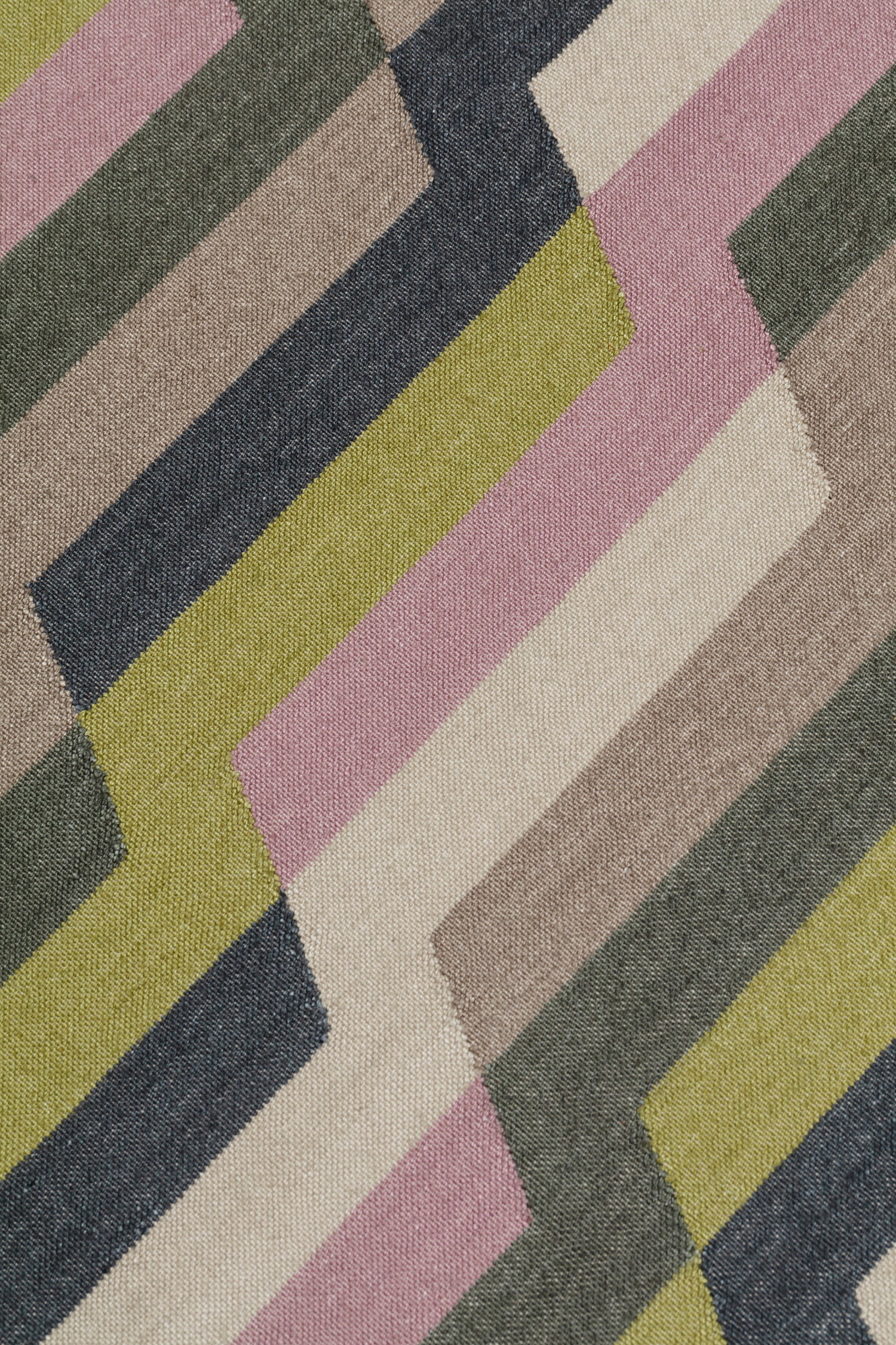 Detail of a handwoven rug with a stacked zig zag stripe in purple, lime green, cream and shades of grey. 
