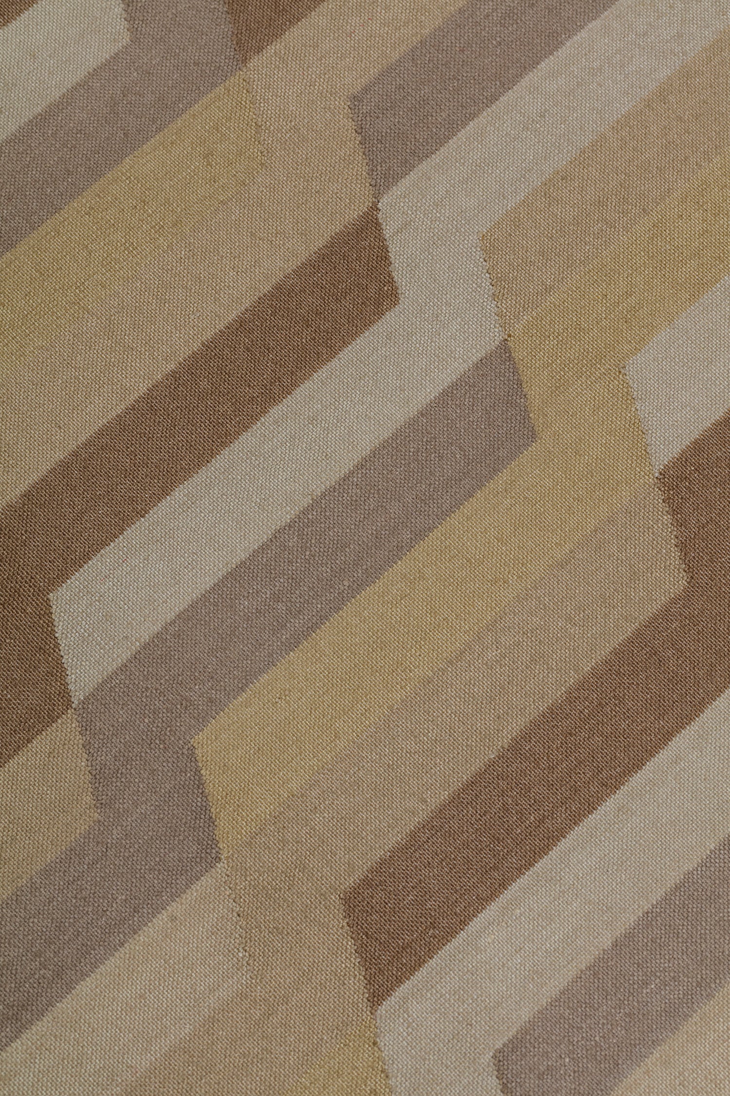 Detail of a handwoven rug with a stacked zig zag stripe in shades of brown, taupe, and tan. 