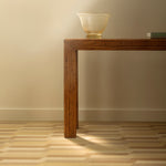 Bamboo console table against a white wall with glass vase and books atop a handwoven rug with a stacked zig zag stripe in shades of brown, taupe, and tan. 