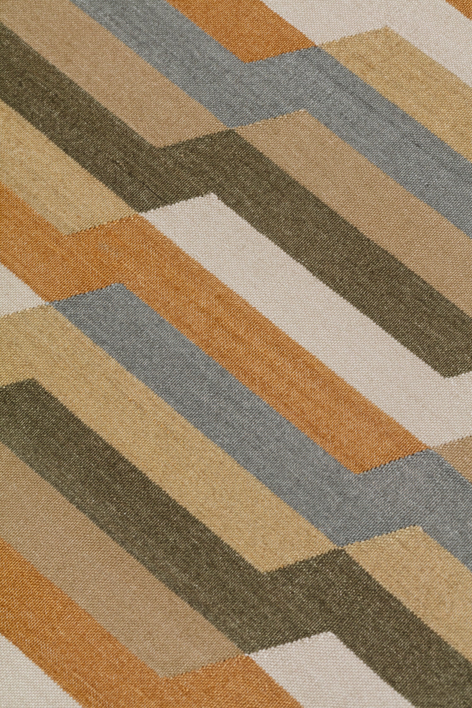 Detail of a handwoven rug with a stacked zig zag stripe in shades of tan, ochre, chambray blue and ivory. 