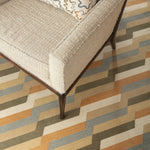 White tweed side chair with an embroidered throw pillow atop a handwoven rug with a stacked zig zag stripe in shades of tan, ochre, chambray blue and ivory. 