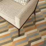 White tweed side chair with an embroidered throw pillow atop a handwoven rug with a stacked zig zag stripe in shades of tan, ochre, chambray blue and ivory. 