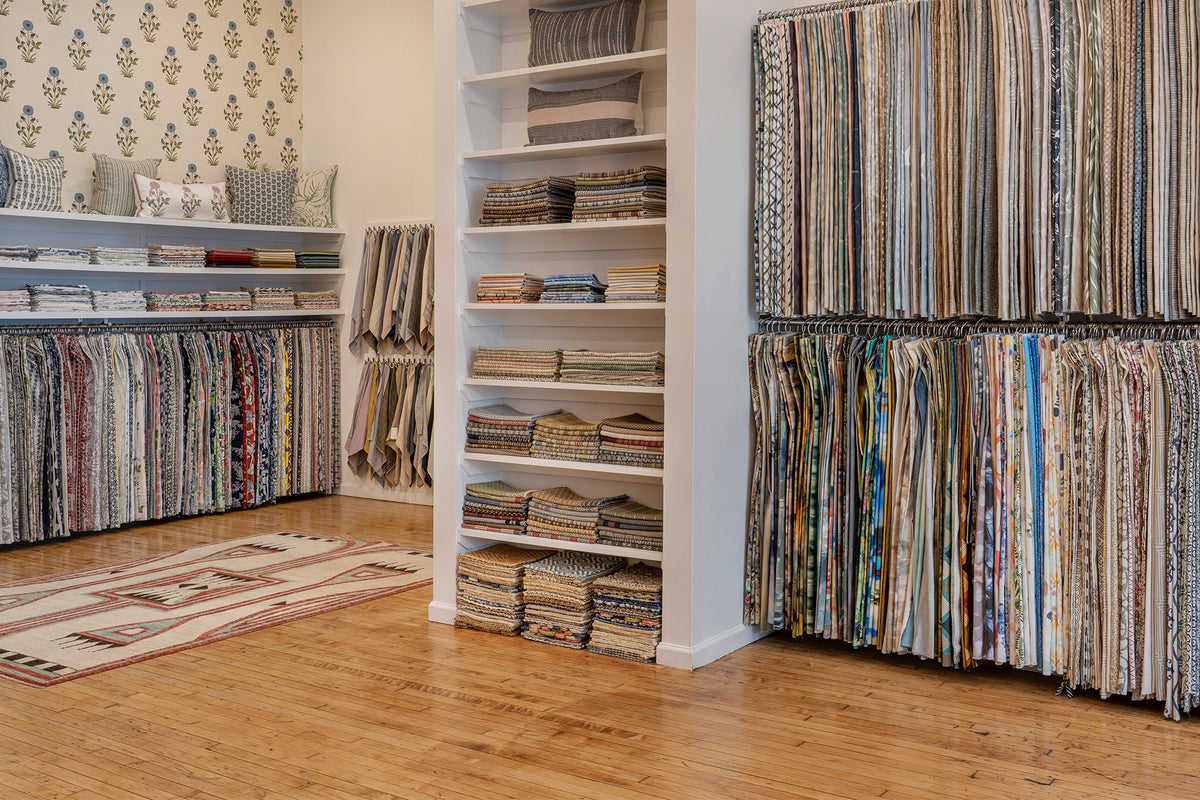 An interior design showroom with hardwood floors, shelves of fabric swatches, and racks full of hanging upholstery fabrics.