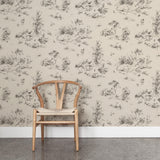 A wooden chair stands in front of a wall papered in a painterly shrub and tree print in charcoal on a cream field.