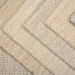 A close-up of overlapping woven rug samples in neutral tones, including beige, cream, tan, and a muted blue-gray, showing the texture and pile of the rugs.