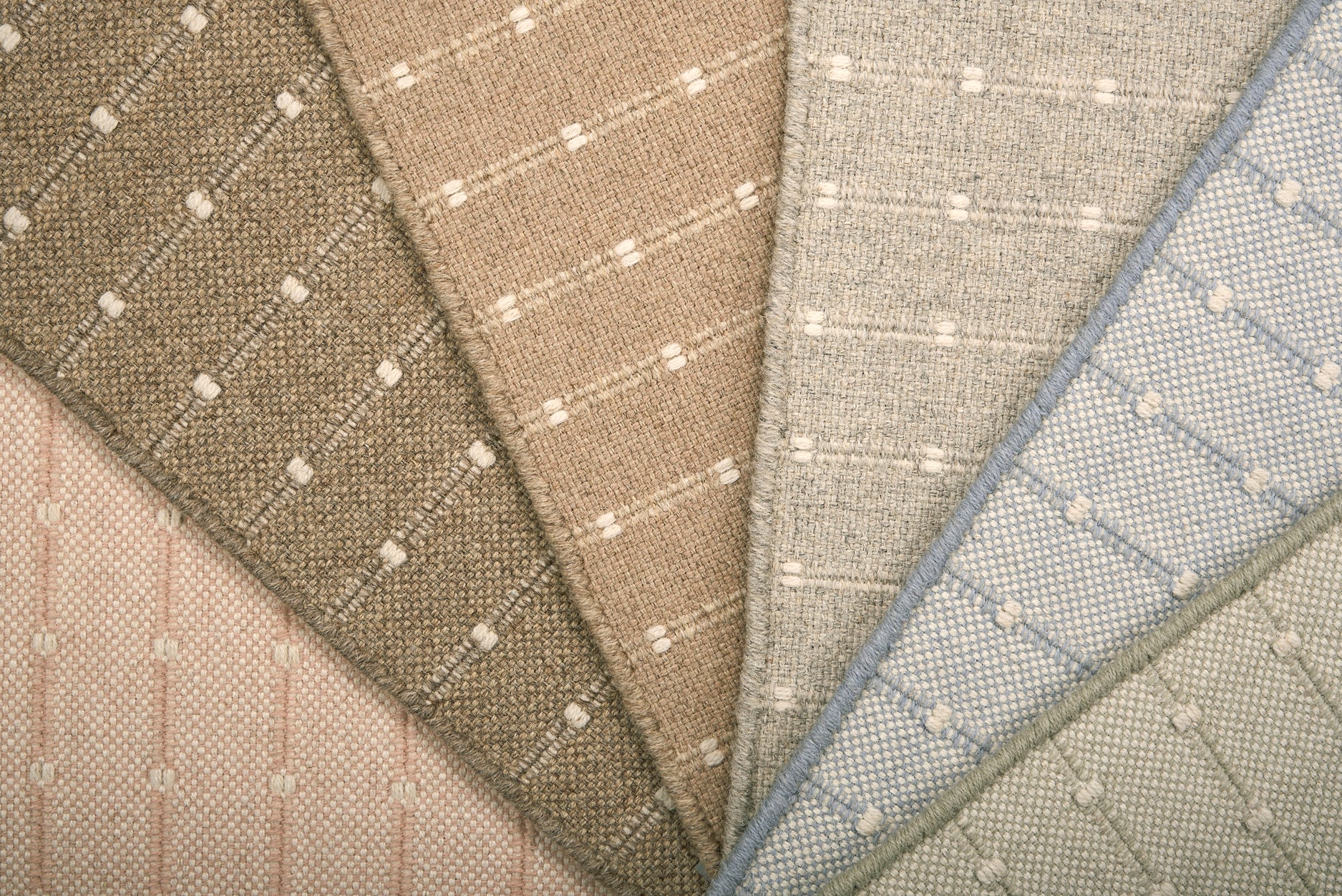 A close-up fan arrangement of striped broadloom carpet swatches in soft neutral and pastel tones, including beige, taupe, light gray, blush pink, and pale blue, each with a subtle stripe pattern.