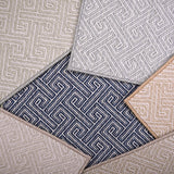 Stack of broadloom carpet samples with a Greek key motif in neutral colors. 
