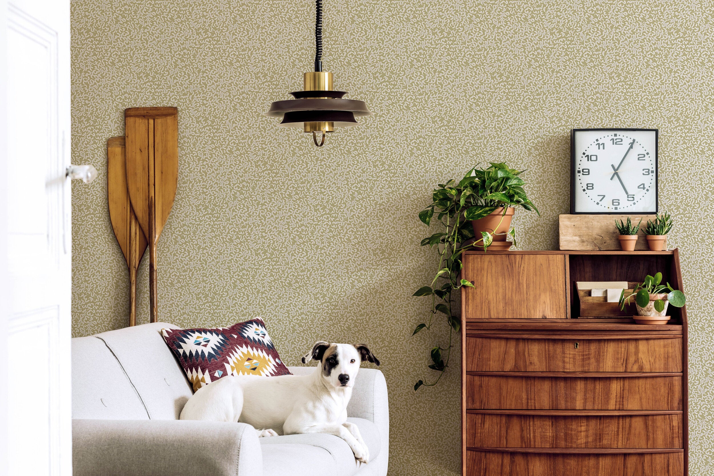 A living room with a dog on a couch and a wall papered in a painterly abstract print in white and mustard.