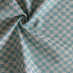 Close up of draped woven fabric with small scale checkerboard pattern in white and turquoise. 