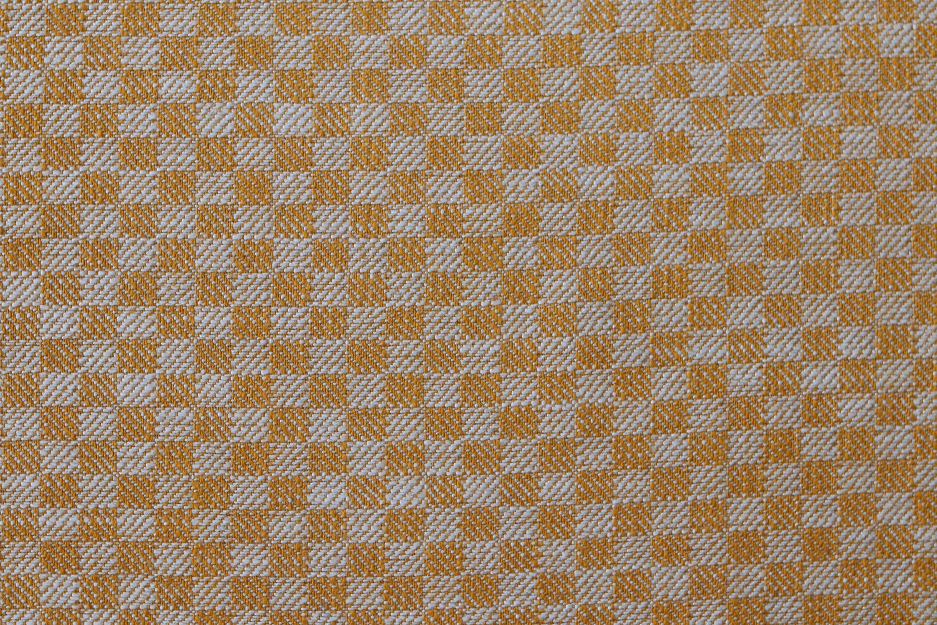 Close up of woven fabric with small scale checkerboard pattern in white and light orange.