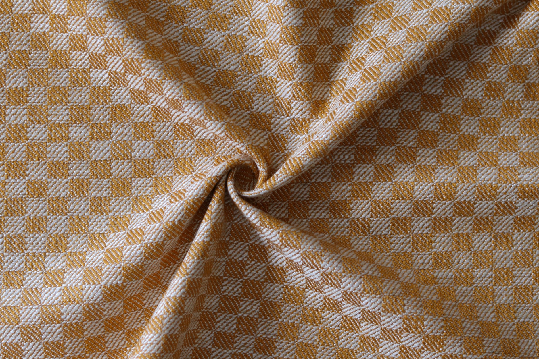 Close up of draped woven fabric with small scale checkerboard pattern in white and light orange.